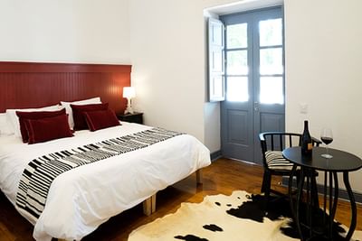 Large bed by a table under a red headboard on a cowhide rug in Deluxe Italian Room at NOI Blend Colchagua