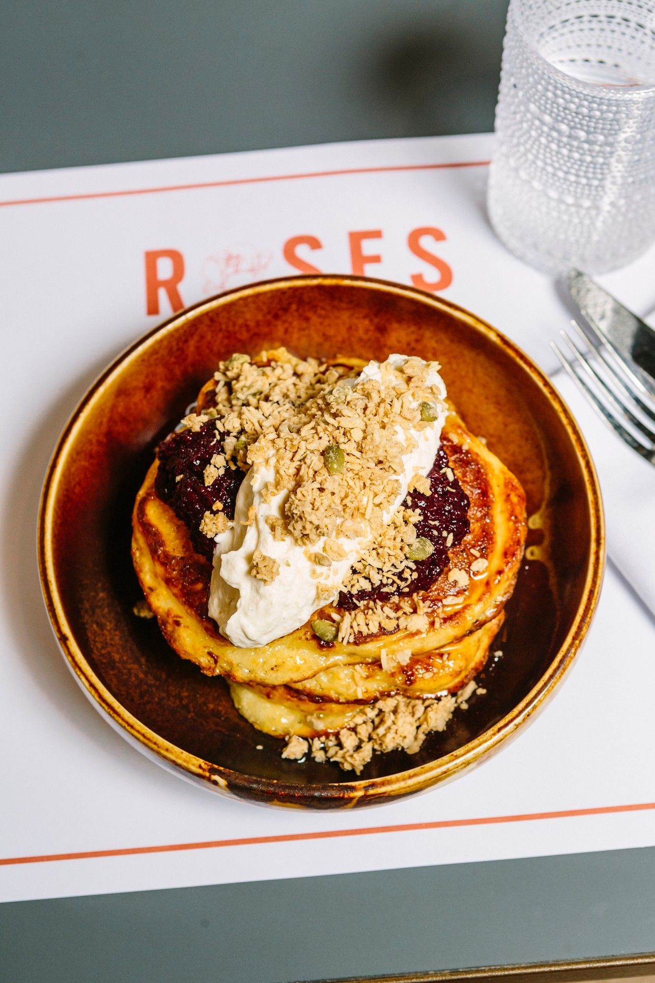 Stack of golden pancakes topped with berry jam and whipped cream and oats in a brown bowl at Hotel X Toronto