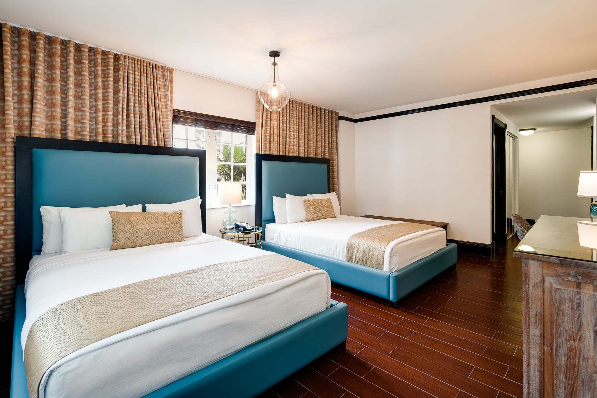 A hotel room with two beds, a window, and a desk.
