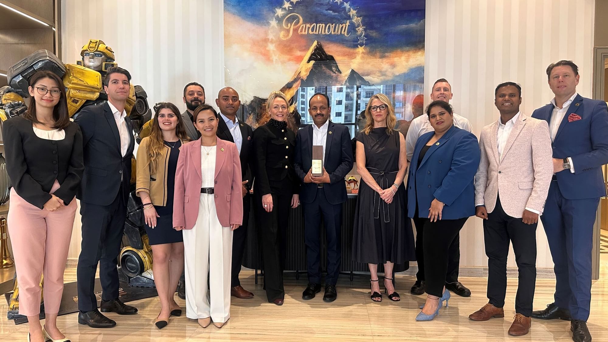 Formally dressed individuals posing with a Bumblebee statue and a Paramount Pictures backdrop at Paramount Hotel Midtown