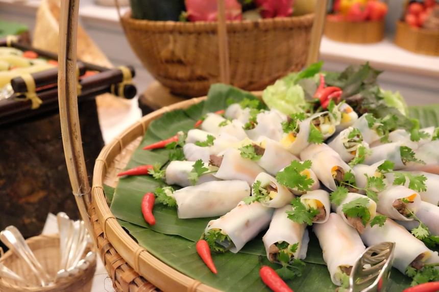 Bamboo basket filled with fresh vegetable spring rolls on banana leaves, garnished with cilantro at Park Hyatt Saigon