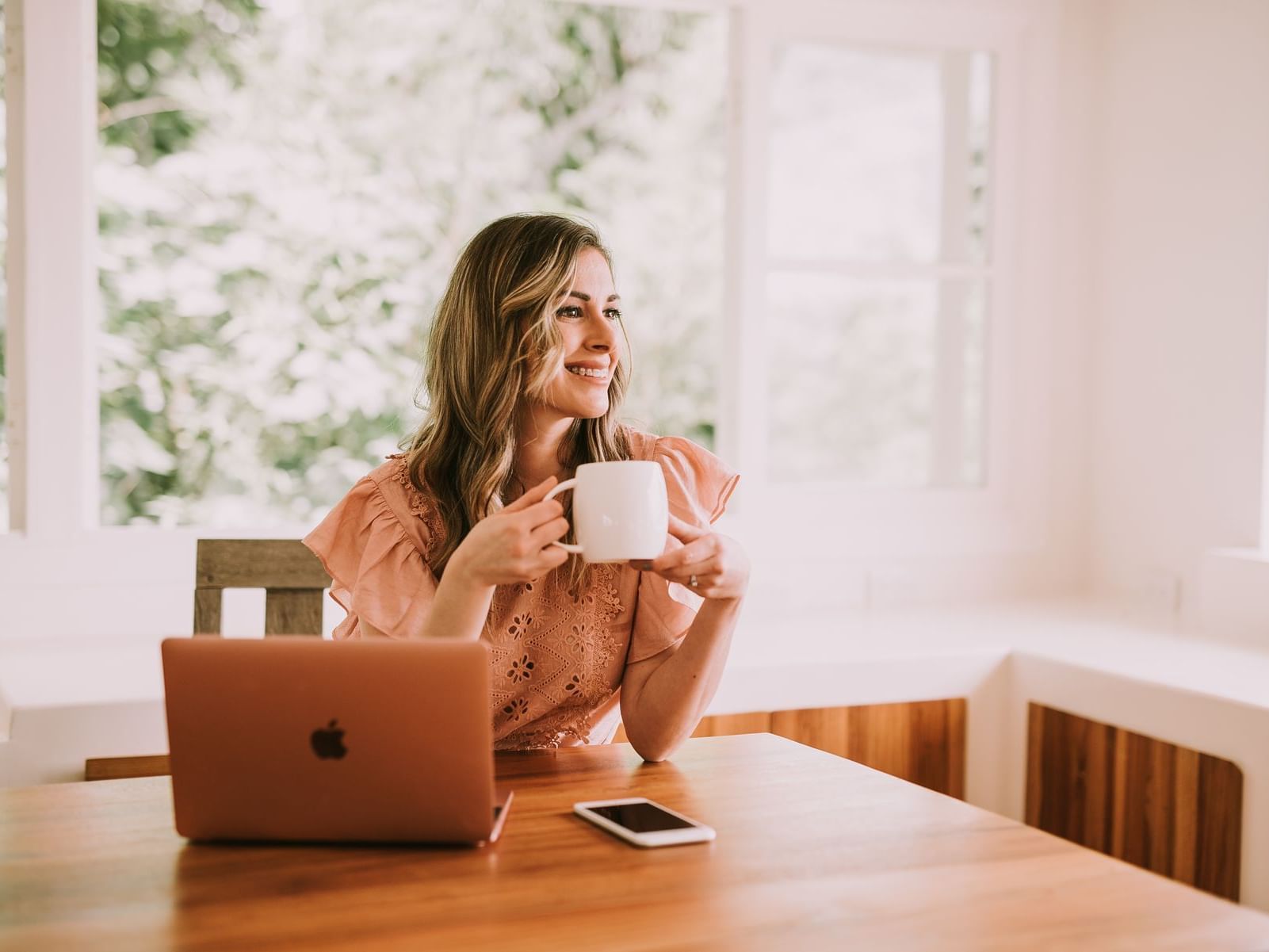 mujer joven sentada sonriendo con taza de café frente a computadora