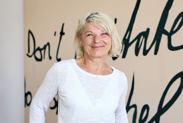 Portrait of a Monika Haider standing in front of a mural with handwritten text at Hotel Motto Vienna