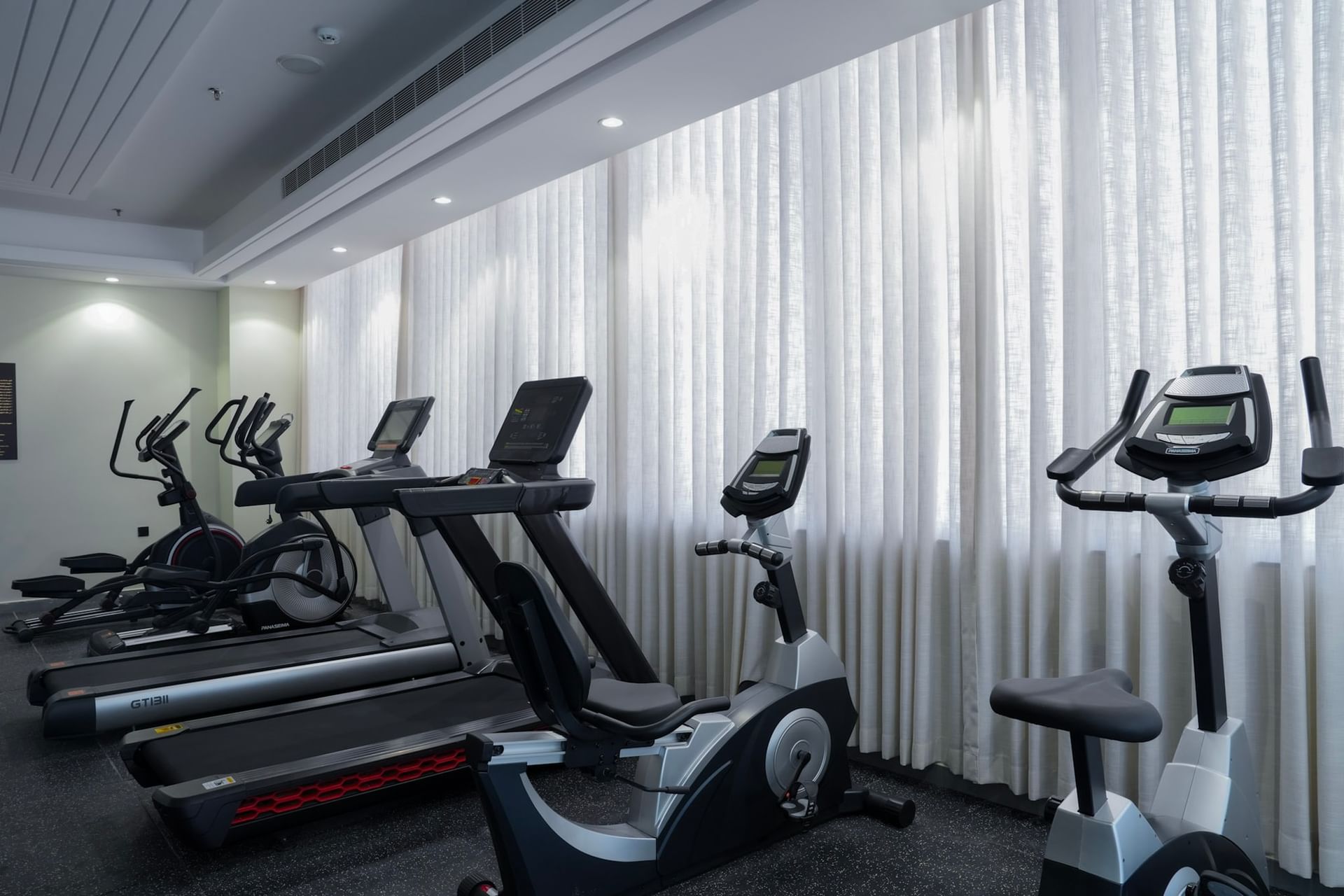 Five exercise machines in a row in a gym with white curtains at Warwick Hotel Spa Jeddah