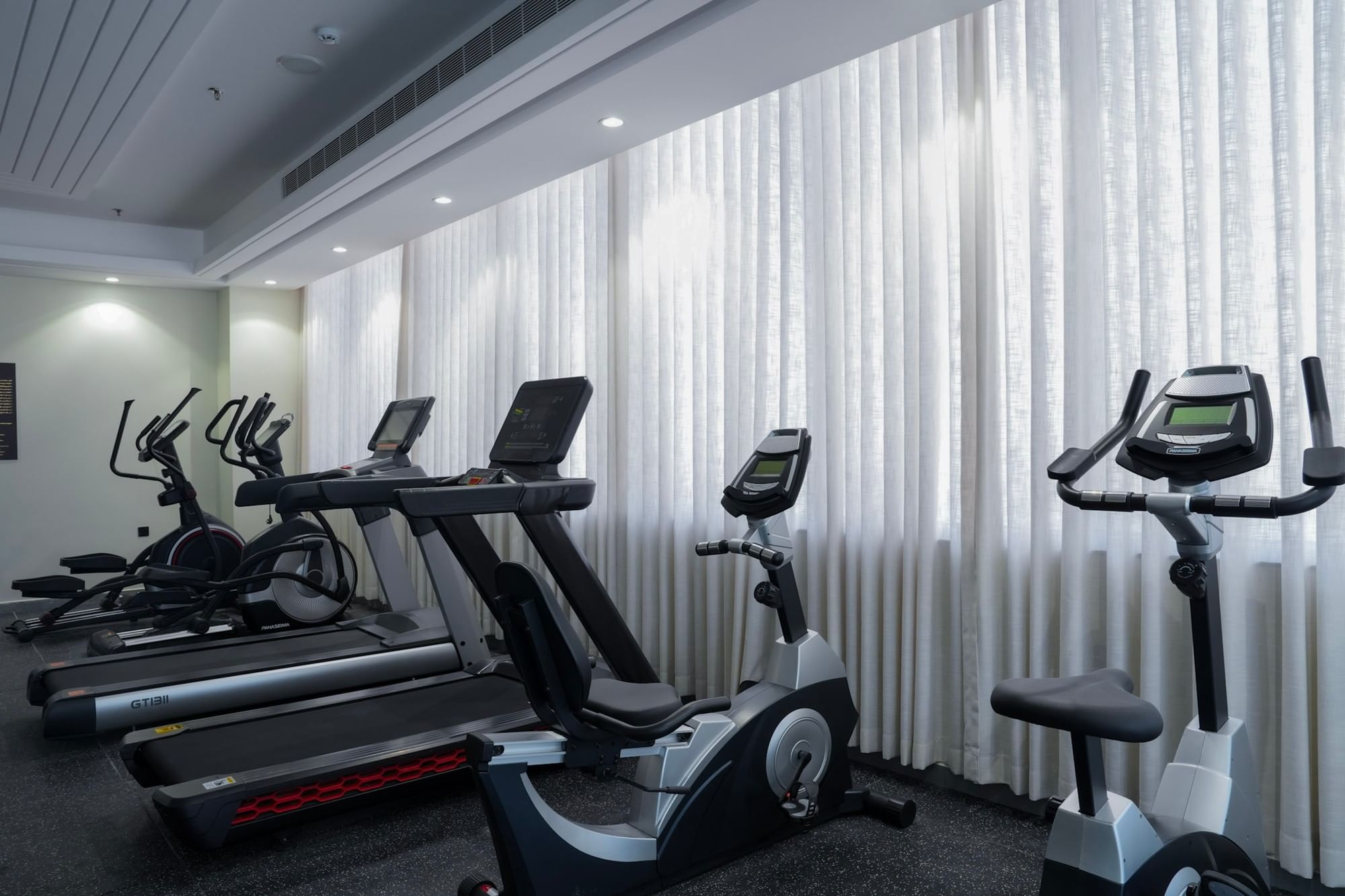 Five exercise machines in a row in a gym with white curtains at Warwick Hotel Spa Jeddah
