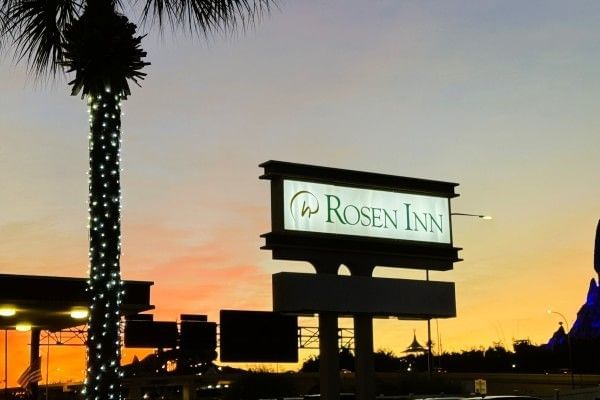 The sign for Rosen Inn against a sunset sky beside a palm tree wrapped in Christmas lights.