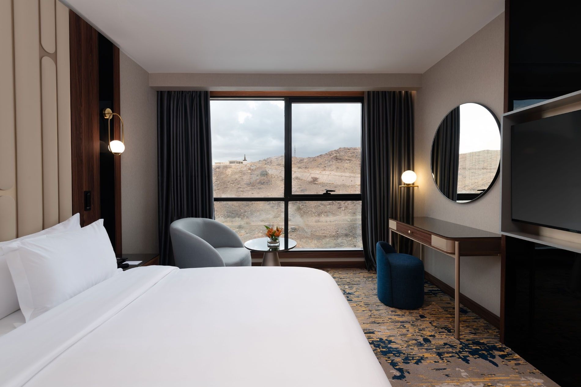 Bed with a couch and a work desk by the window in Junior Suite at Warwick Al Taif Hotel