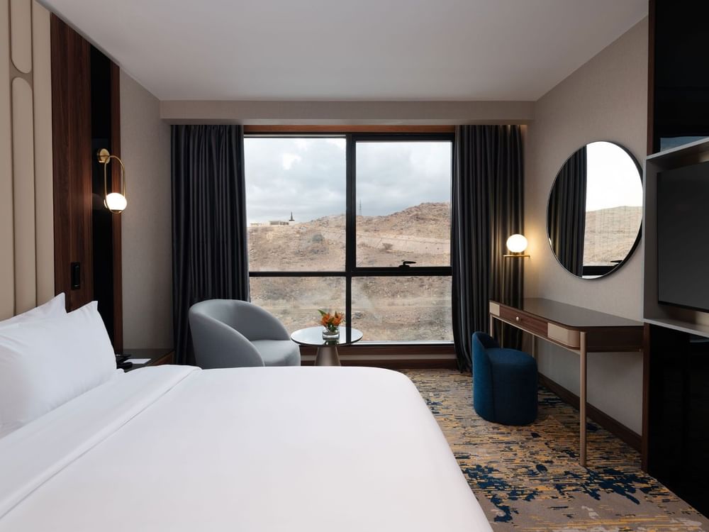 Bed with a couch and a work desk by the window in Junior Suite at Warwick Al Taif Hotel