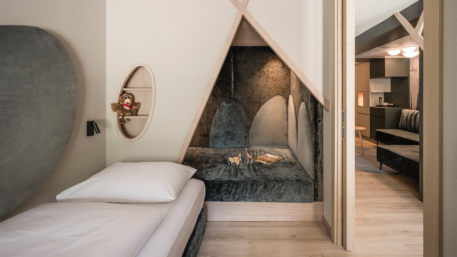 Moderner Schlafbereich mit Bett, Wandnischen, Couch und separatem Spielbereich.