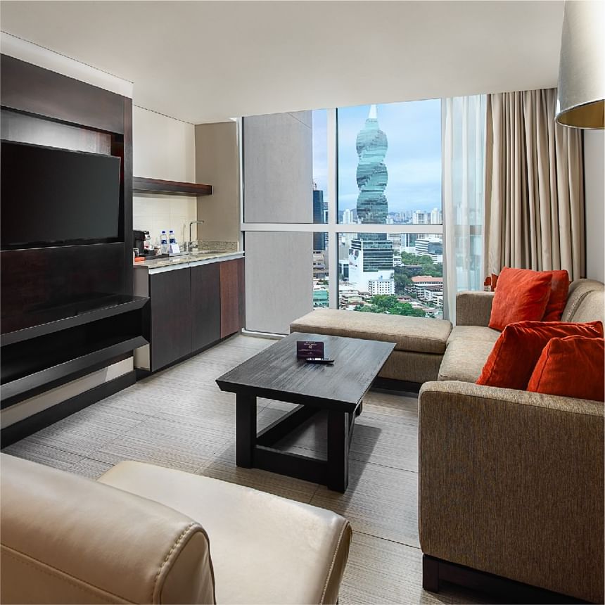 Sala de suite moderna con sofá y televisor frente a vistas de rascacielos en Megapolis Hotel Panama