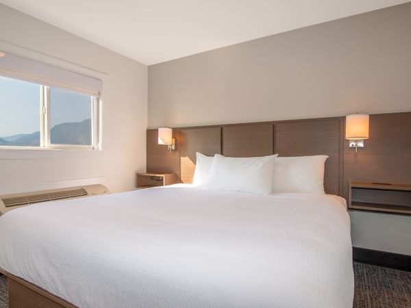 A hotel room with a large bed, two lamps, and a window.