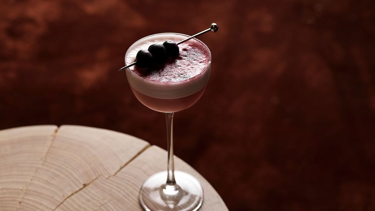 Cocktail in a martini glass with black olives on a stick, on a wooden table.