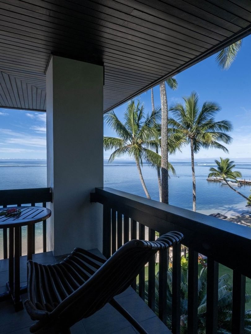 Wooden chairs by a table under a dark ceiling on a balcony with palm trees in Warwick Suites at Warwick Fiji Resort and Spa