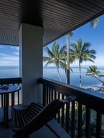 Wooden chairs by a table under a dark ceiling on a balcony with palm trees in Warwick Suites at Warwick Fiji Resort and Spa