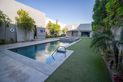 Narrow swimming pool by a stone patio under a clear blue sky surrounding an artificial grass lawn area at Hotel Mirra