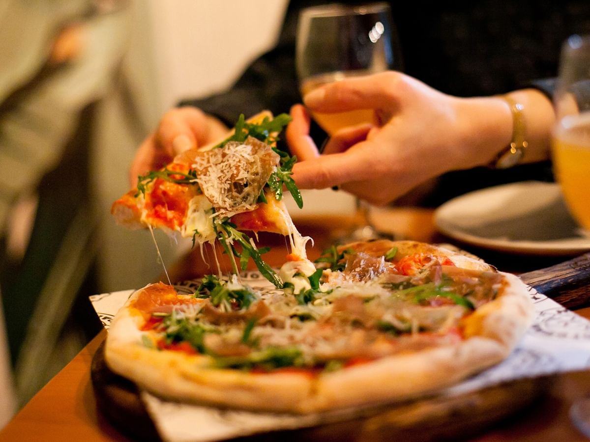 Guest enjoying a slice of fresh flatbread pizza with arugula and beverages at Coast Langley City Hotel & Convention Centre