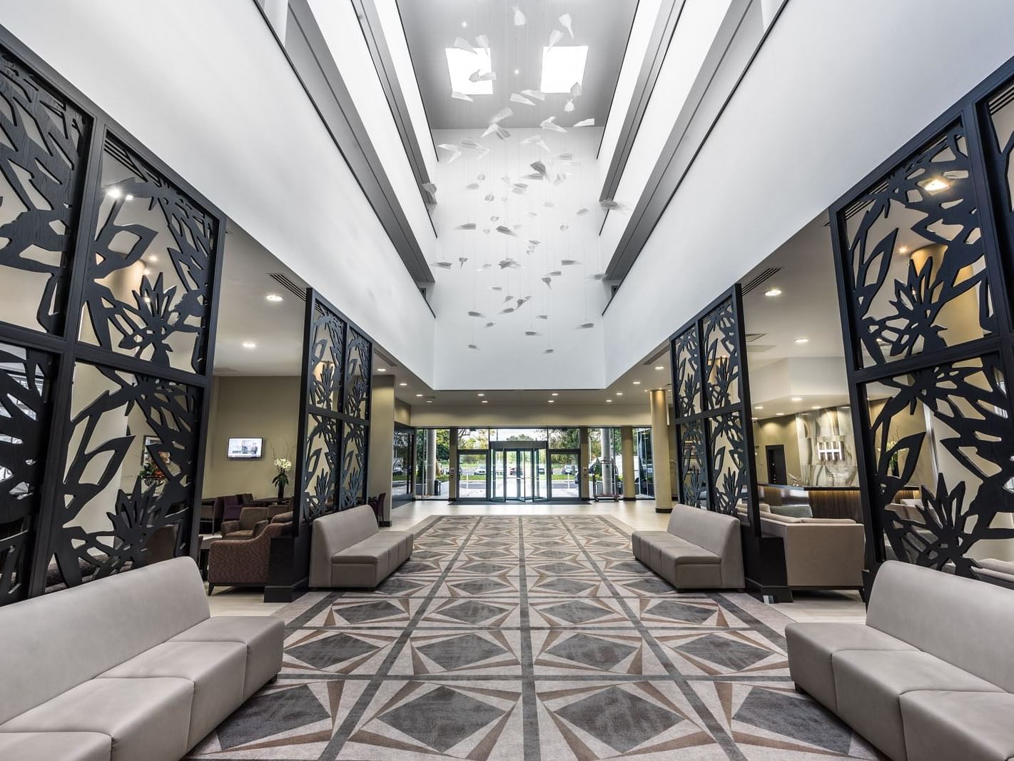 Lobby with high ceilings, patterned carpet, chic seating, and black decorative screens by the entrance at Heston Hyde Hotel