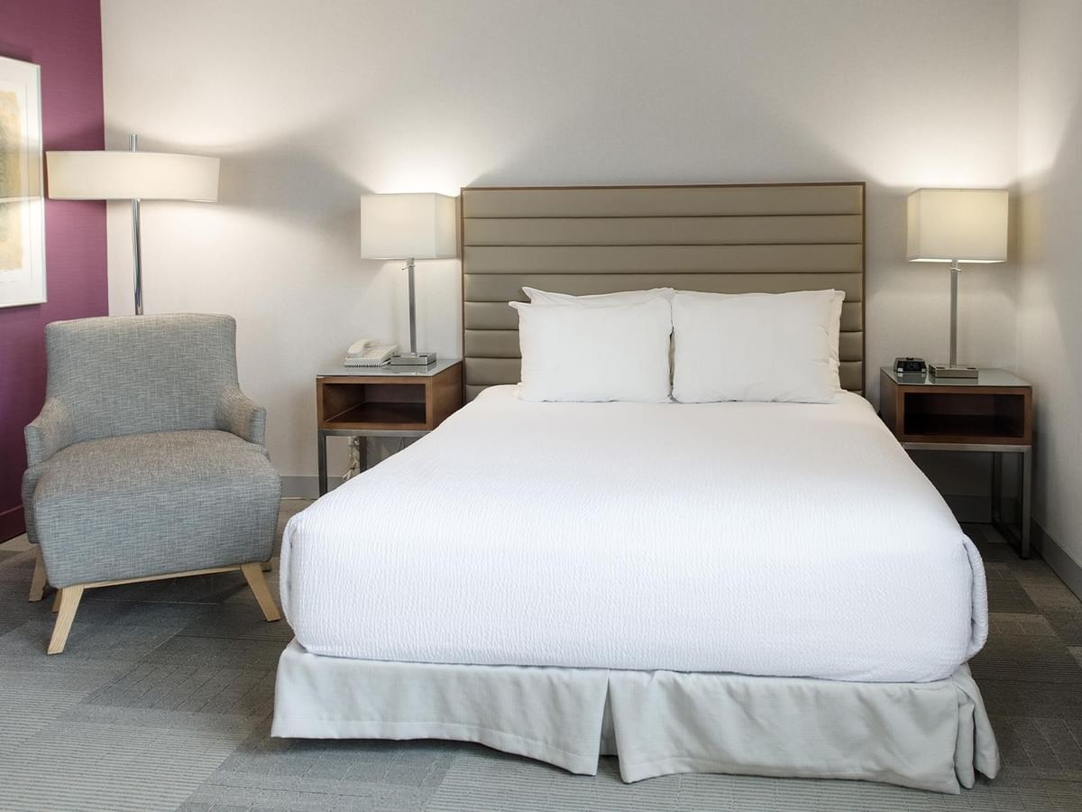 Queen bed with gray upholstered headboard, armchair, and nightstands in Coast Accessible Queen Junior Suite at Coast Prince George Hotel.
