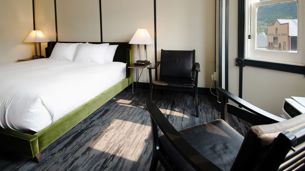 Hotel room with king bed, lamp, night stand, chair, and window