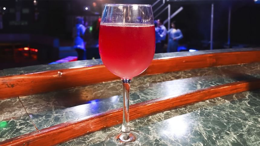 Copa de cóctel de vino tinto en barra de madera frente a pista de baile iluminada en El Rollo en Araiza Palmira
