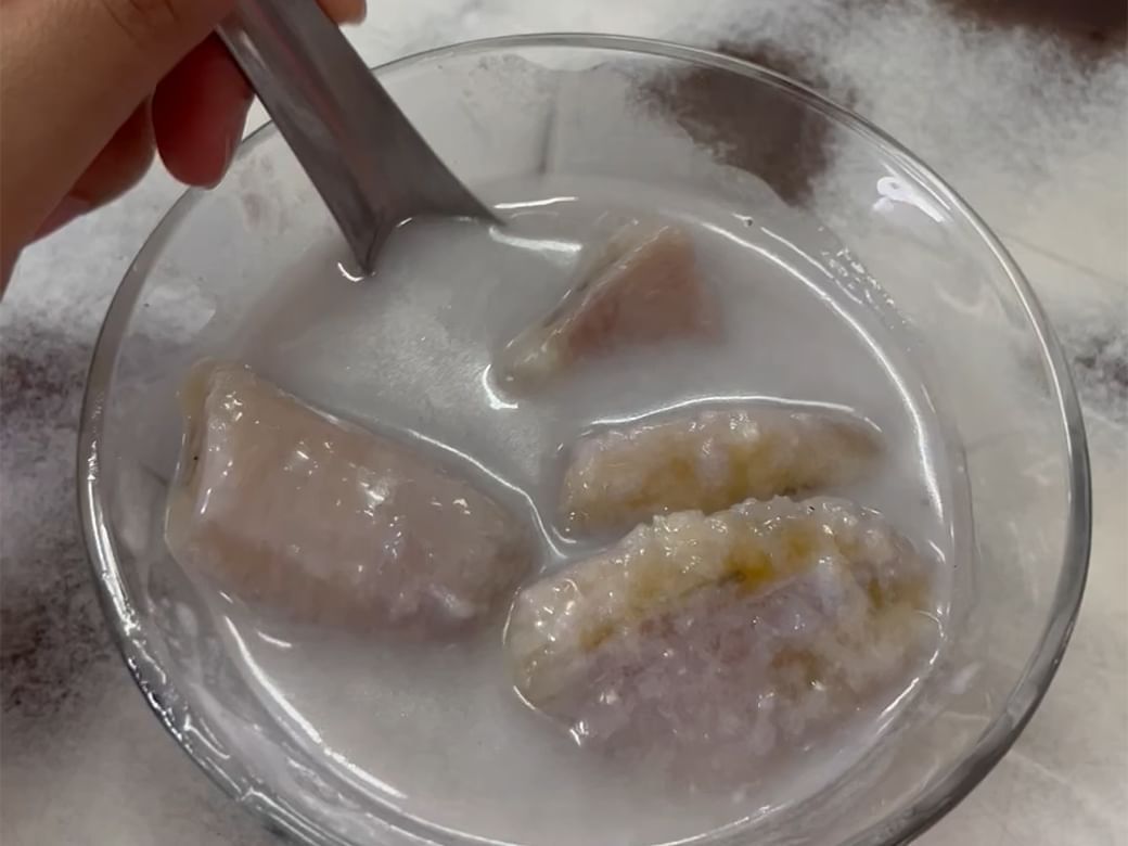 Hand stirring a bowl of bananas and taro in a creamy coconut dessert at Hop Inn Hotel