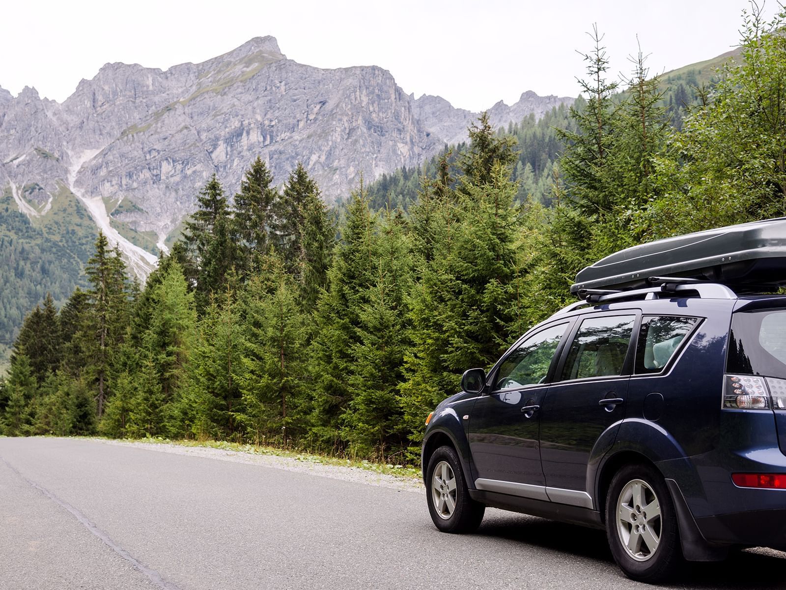An image of a car on the road near a forest and mountains