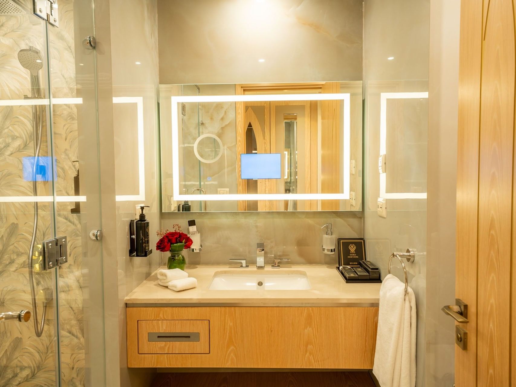 Modern bathroom with glass shower, wooden vanity, and illuminated mirror at World Heart Hotel Baghdad.