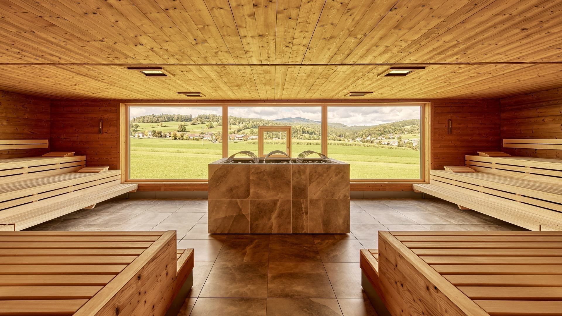 Moderne Sauna mit Holzbänken und Panoramafenster mit Blick auf grüne Landschaft im Falkensteiner Hotel Bad Leonfelden