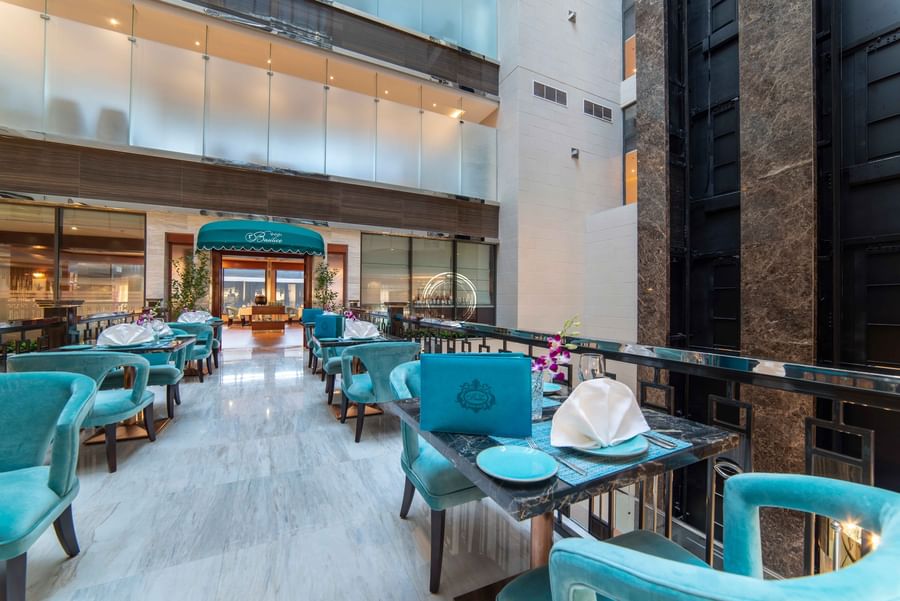 Italian restaurant with teal chairs and white napkins by a black railing overlooking an atrium at Warwick Al Khobar