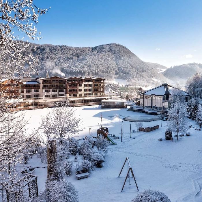 Winter landscape with snow-covered buildings and playground against mountains near Falkensteiner Family Resort Lido 