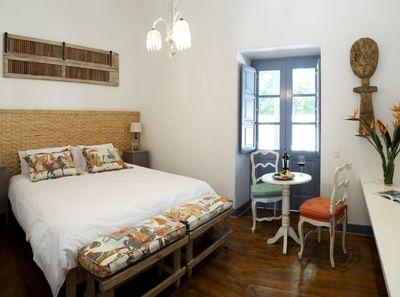 Wine by a bistro table & chairs under a crystal light near a bed with a wicker headboard in room at NOI Blend Colchagua