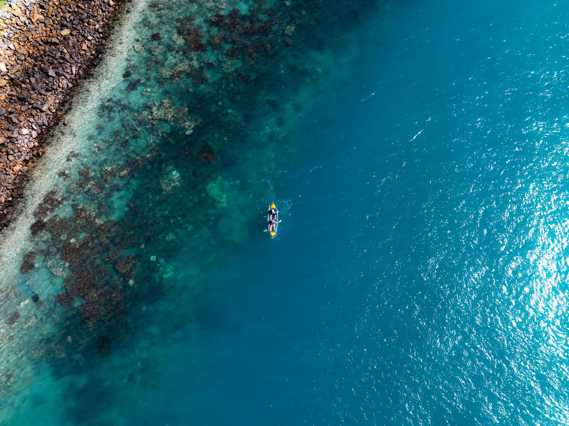 Top-down aerial view of a person paddle boarding over the colorful shallow reef near the shore of Daydream Island