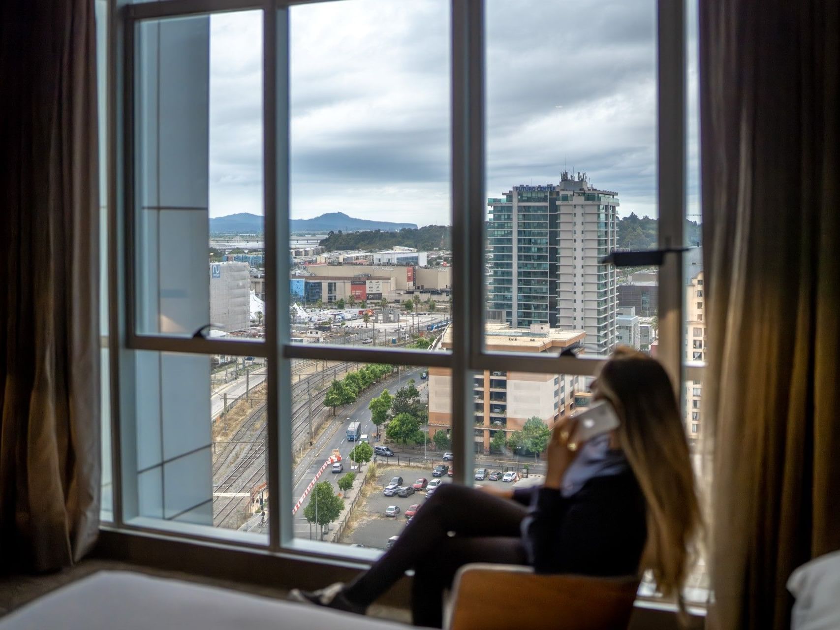 Mujer con el móvil en la mano en una habitación de hotel con vistas a la ciudad.