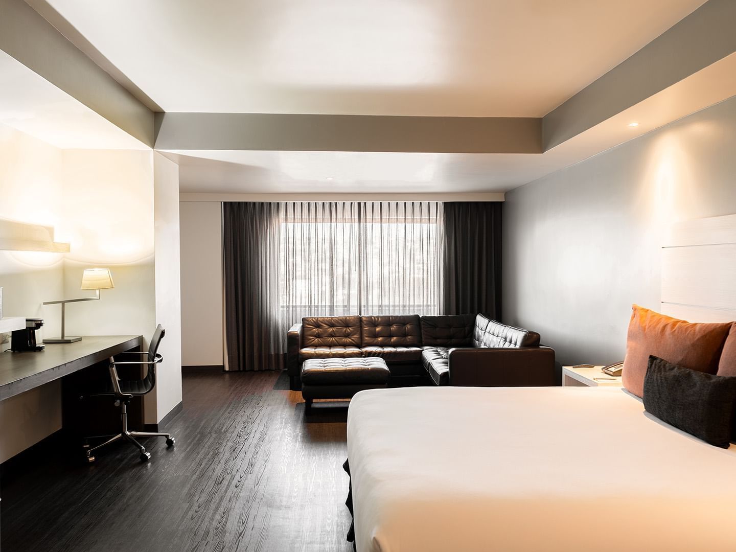 Workspace and black leather sectional by the cozy bed in the King Junior Suite with wooden floors at Real Inn Tijuana