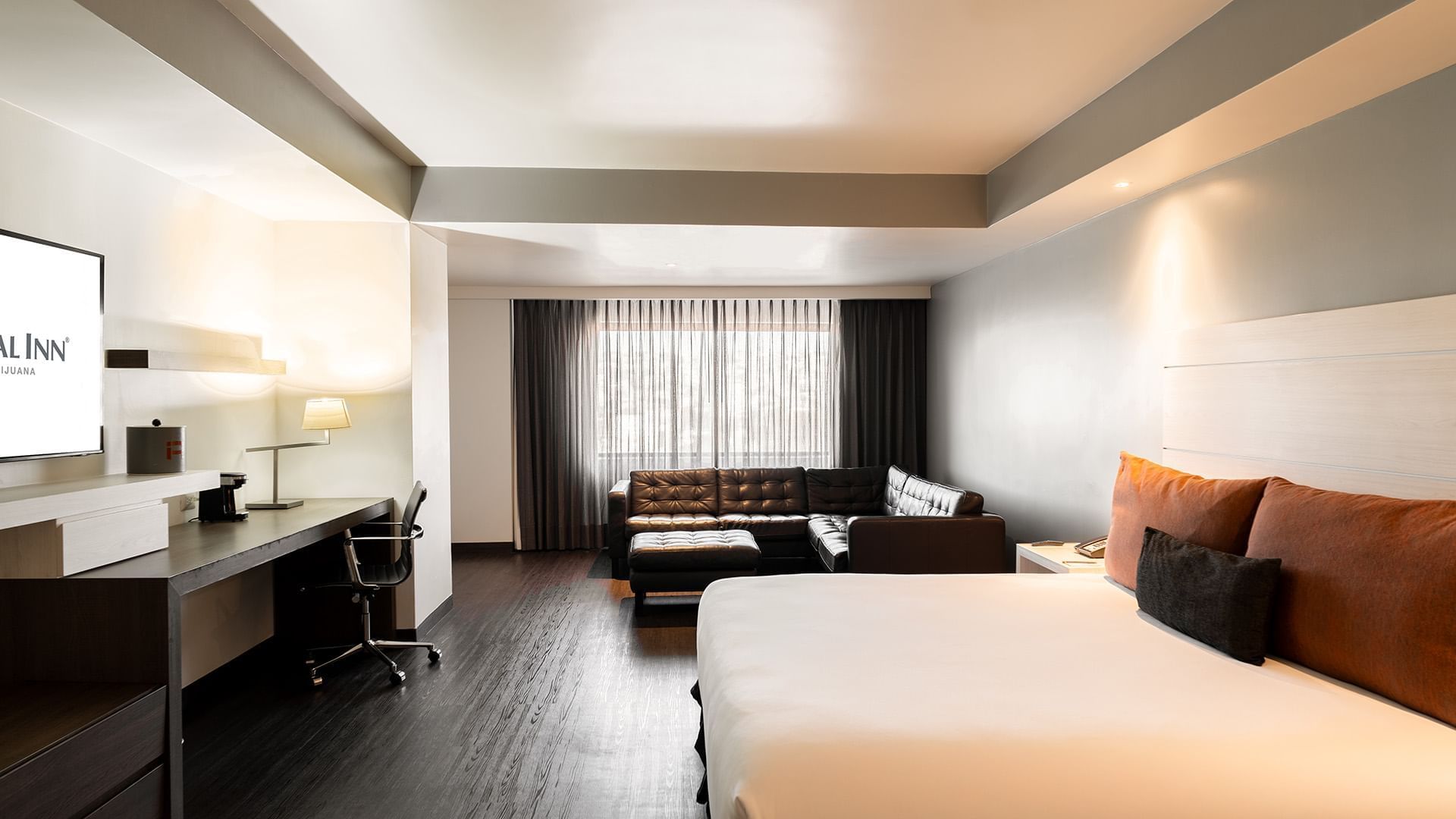 Workspace and black leather sectional by the cozy bed in the King Junior Suite with wooden floors at Real Inn Tijuana