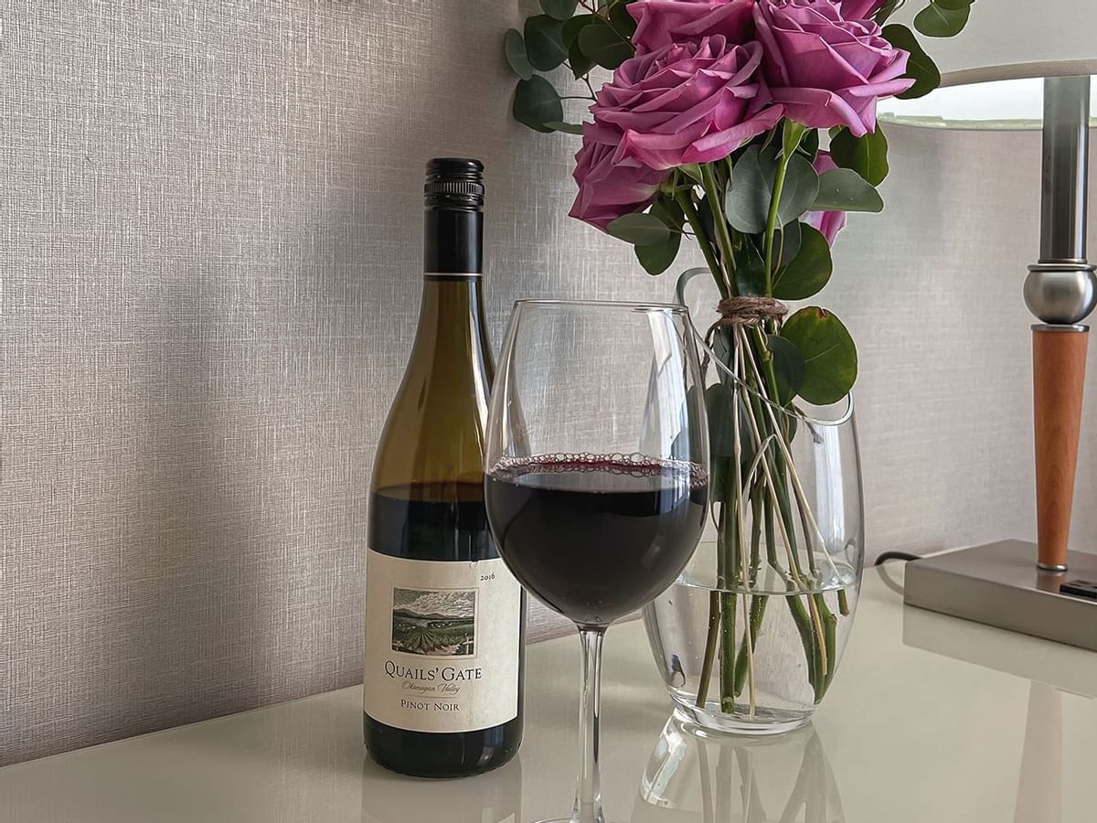 Wine bottle and wine glass with vase of roses on counter top