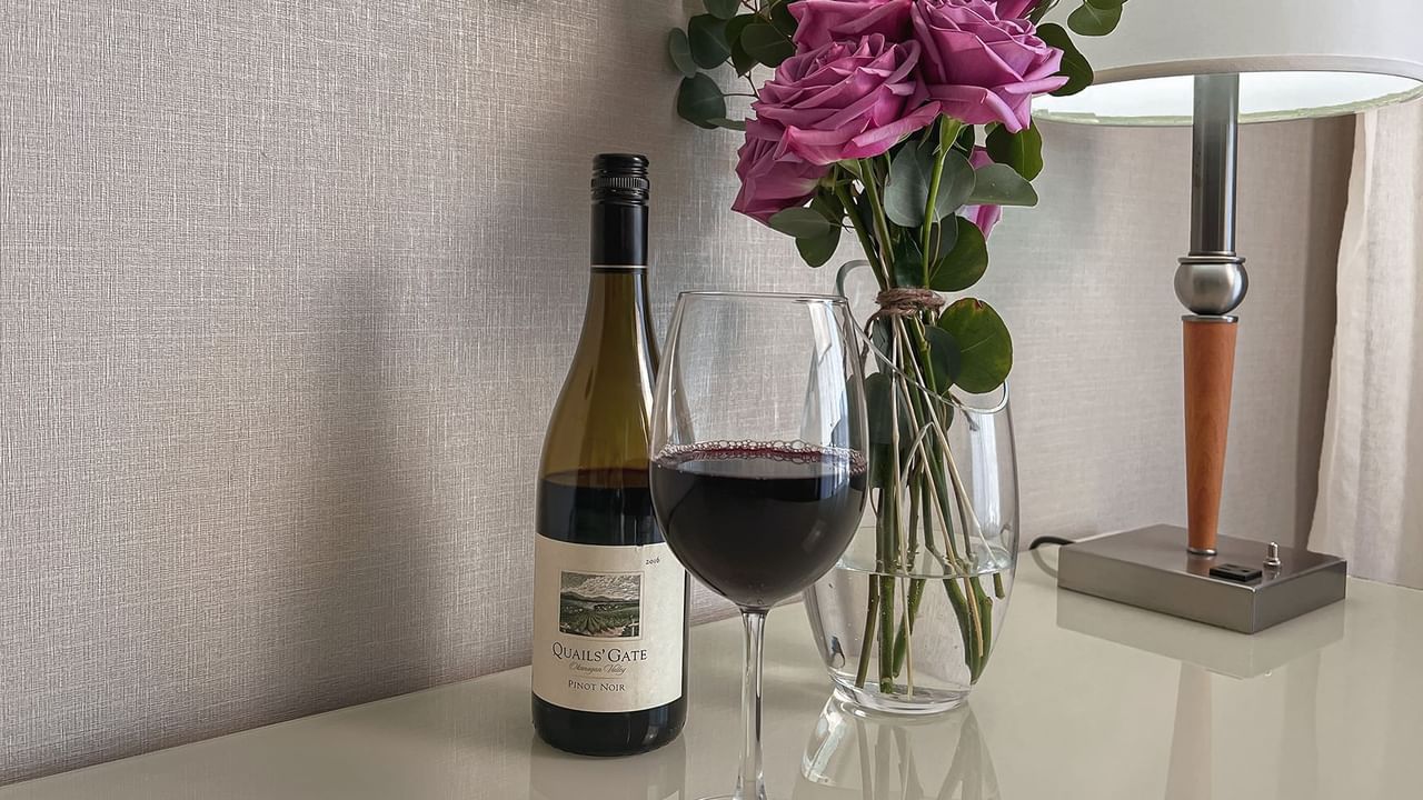 Wine bottle and wine glass with vase of roses on counter top