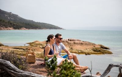 Couple sitting on a rock while enjoying drinks at the Bay near Freycinet Lodge