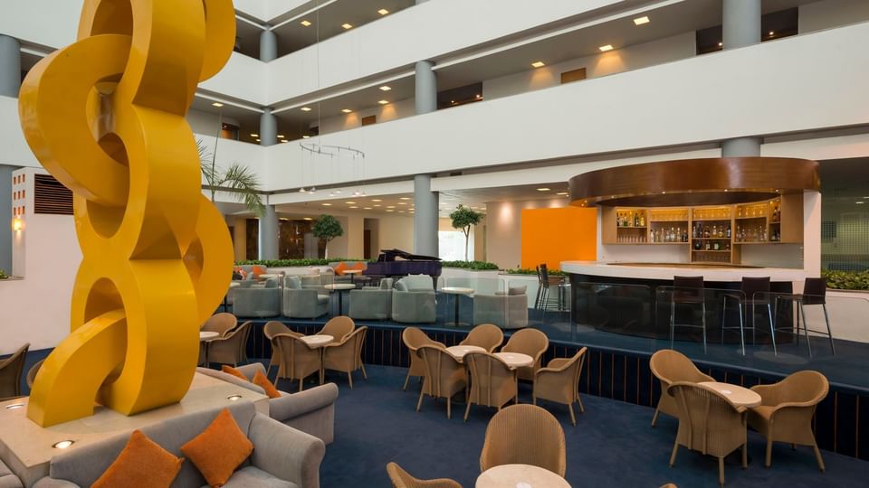 Lobby Bar featuring a large yellow sculpture, blue carpet, and a circular wooden counter at Real Inn Nuevo Laredo