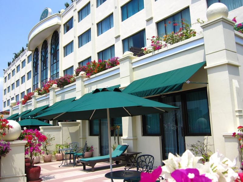 The exterior of Sunway Hotel Phnom Penh with a sunny outdoor terrace adorned with lush flowering plants and green umbrellas