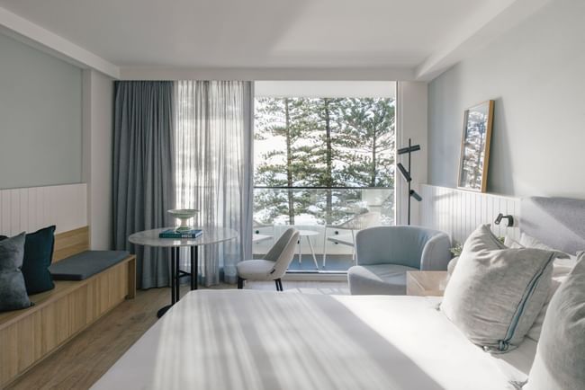 Elysium Manly room featuring a cozy bed and marble table with pine tree views, offering places to stay in Manly