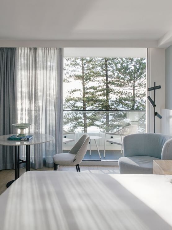 Ocean View Two Bedroom at Elysium Hotels, bed facing a round table, chairs, and balcony framed by pine trees
