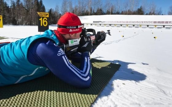 Biathlete on a mat by target lanes under a bright blue sky during winter training near High Peaks Resort