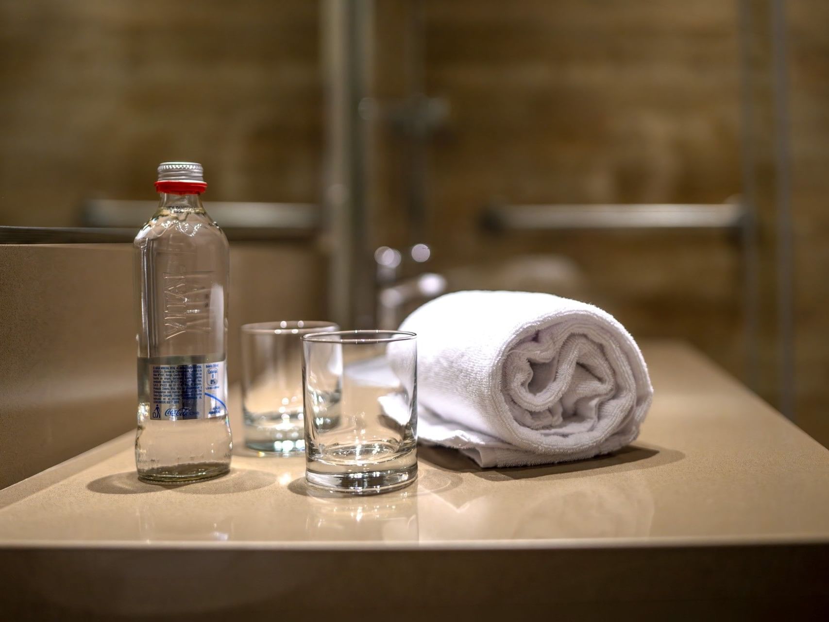 Una botella, dos vasos y una toalla sobre el lavabo del baño del hotel HCC Costanera Concepción.
