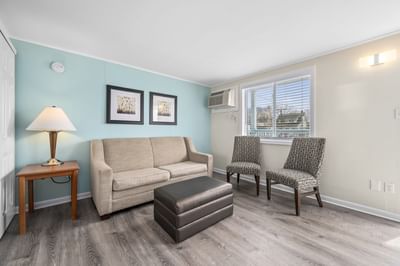 Deluxe Queen Suite living area featuring a beige sofa, two patterned chairs, a table, and a lamp at Madison Beach Motel