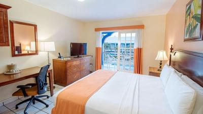 Superior Room King featuring a king-size bed, desk, TV, and balcony doors with outdoor views at Bay Gardens Inn
