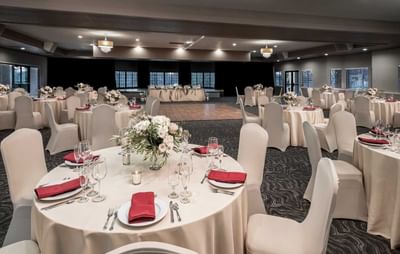 Elegant ballroom with round tables dressed in white linens, red napkins, and white floral centerpieces