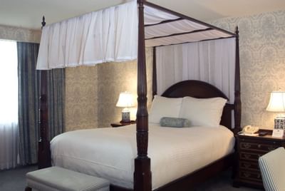 Canopy four-poster bed with bedside lamps and a bench in the Deluxe Room at Farmington Inn and Suites