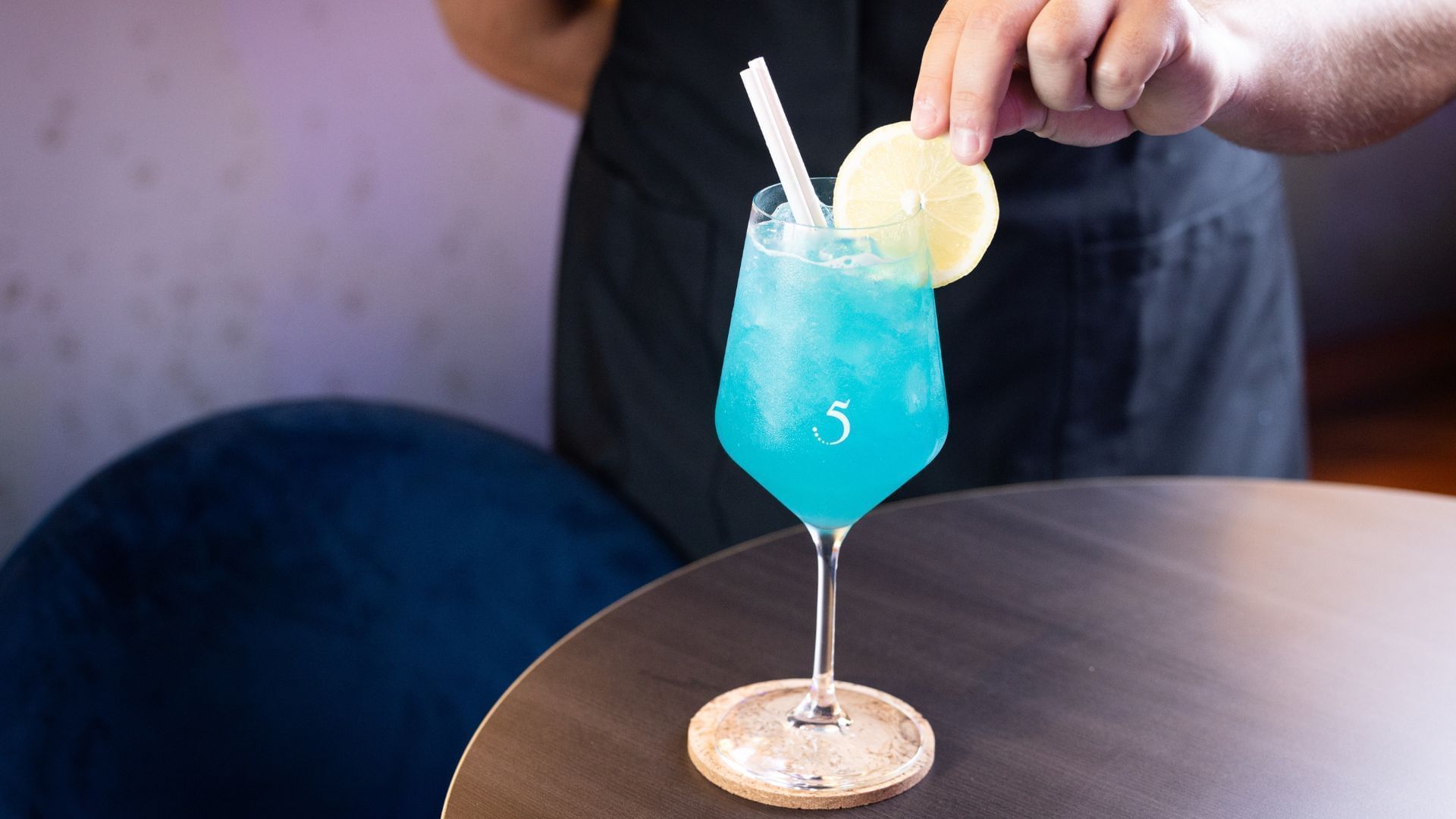 A person places a lemon slice on a refreshing blue cocktail with a straw at Novotel Perth Langley's bar