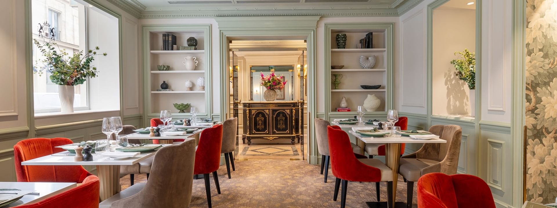 Le Céladon dining area with tables surrounded by red & beige velvet chairs, by built-in shelves at Hotel Westminster Paris